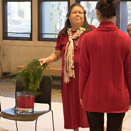 Tribal Elder dips cedar branches in water while greeting a staff member