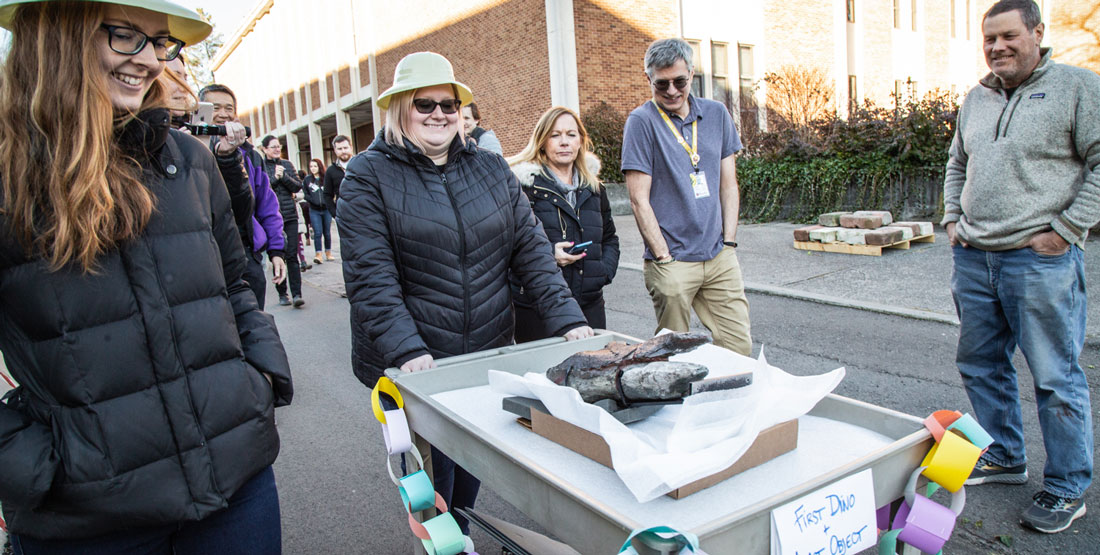 a team rolls the last object--a dinosaur fossil--on a cart as other staff cheer them on