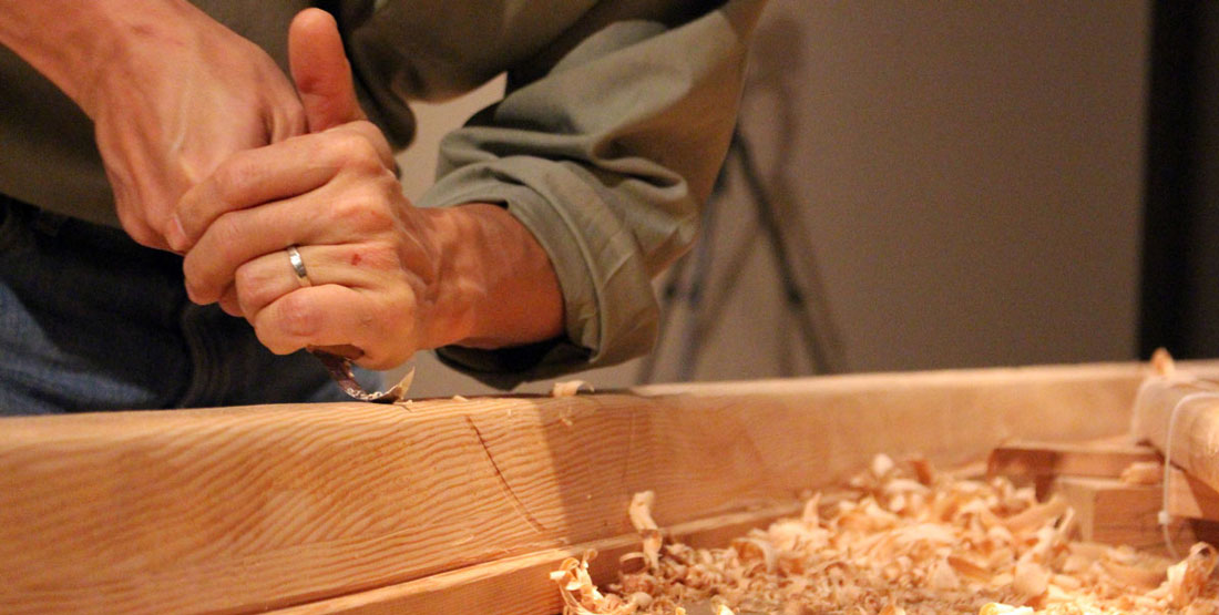 Hands using a hand tool to carve into the wood of a madrone tree