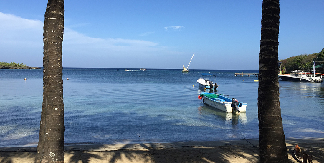 a beach with calm water and several boats anchored offshore