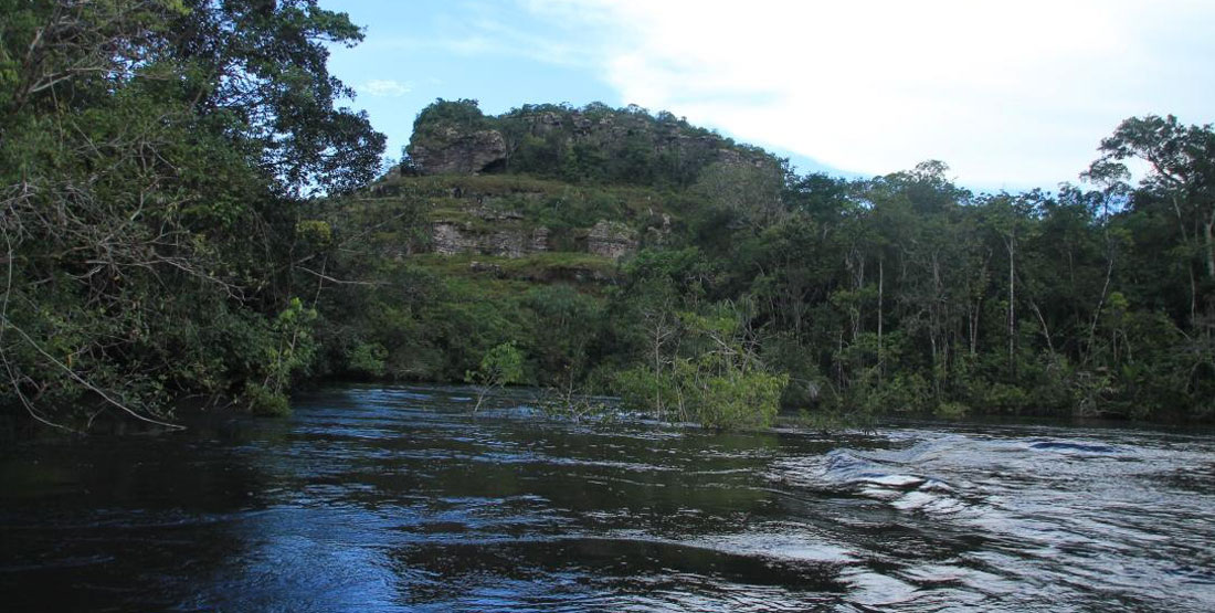 A river with vegitation on both sides and giant outcrop of rock