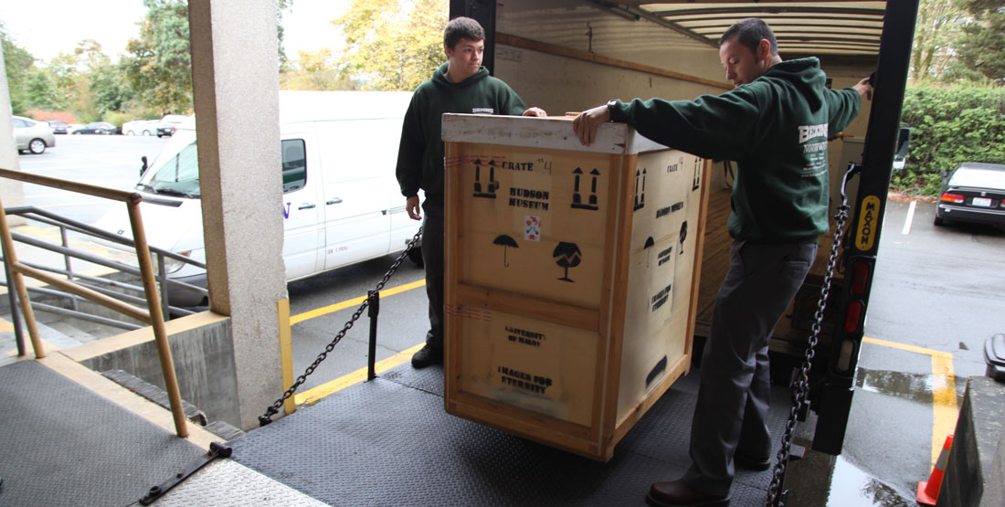 Two men unload a packing box from a truck