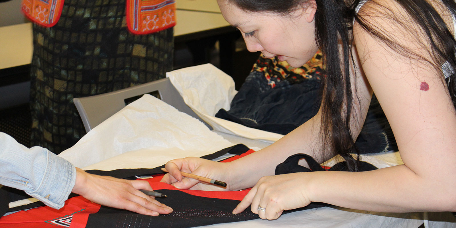 a woman holds a pencil while touching a hmong textile and examining its details