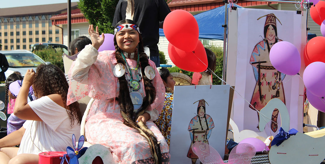 a teenage girl wearing traditional Yakama Nation attire waves from a parade float