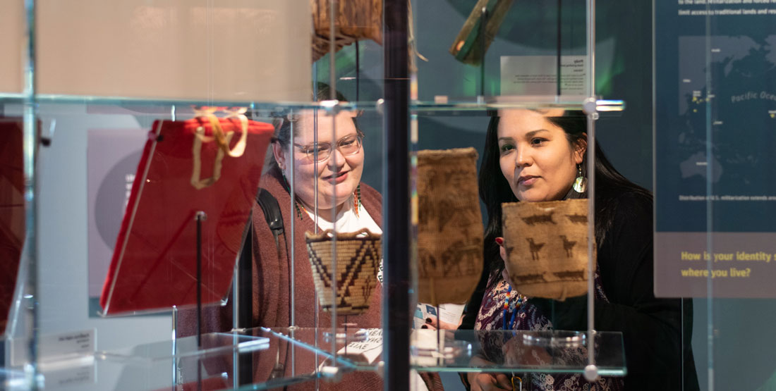 Two women look at a basketry item on glass shelving