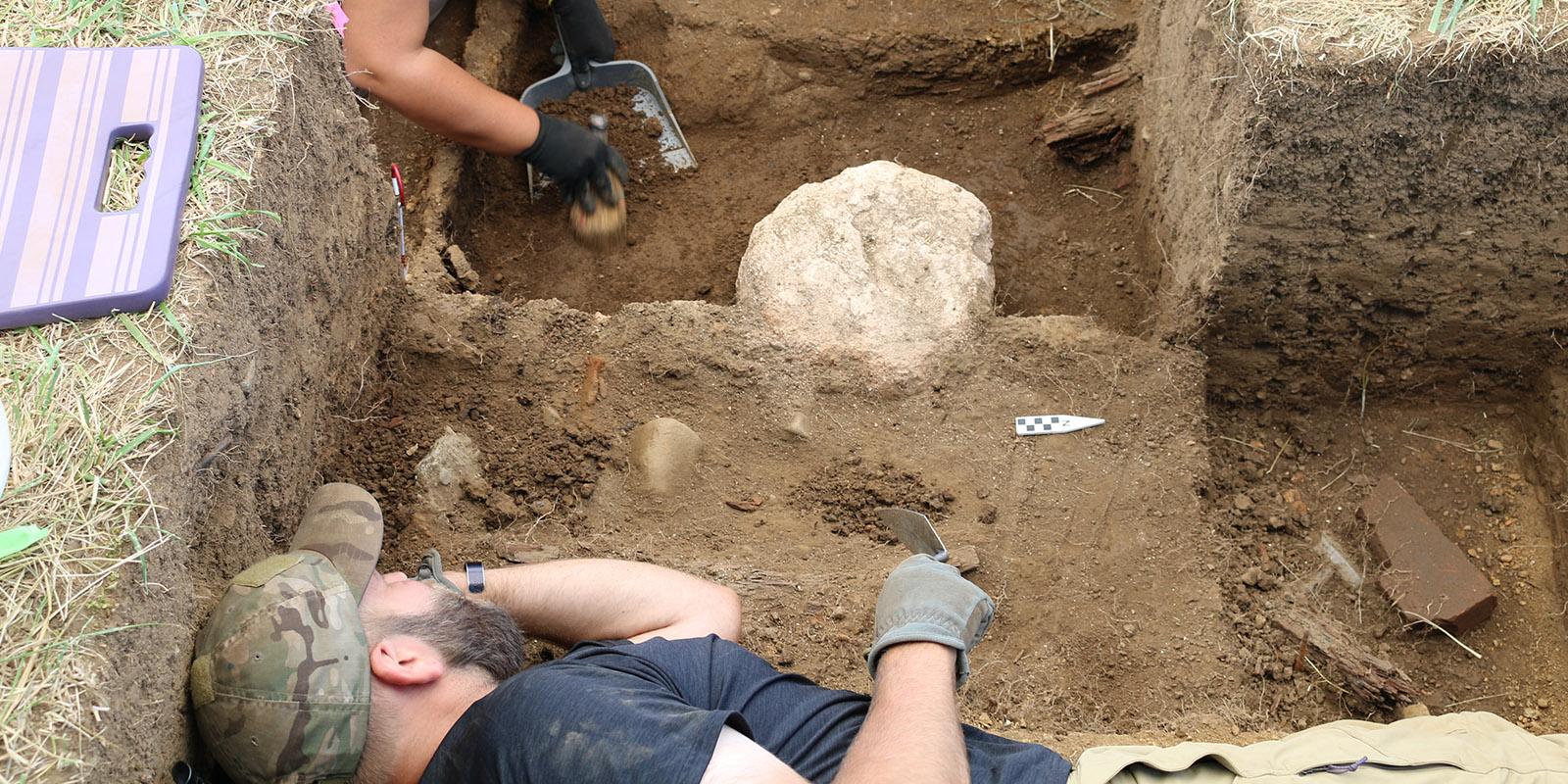 A man digs in a pit with rock artifacts around him