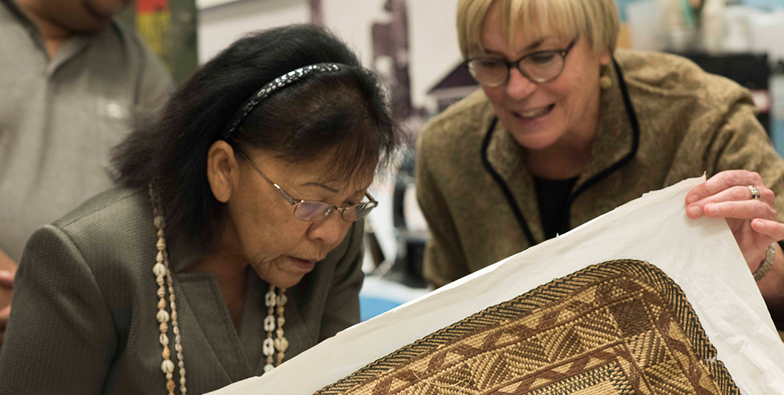 Two women look at a woven textile