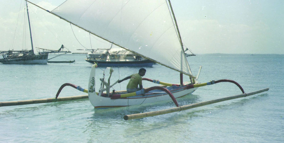 A man in an outrigger sail boat on the water
