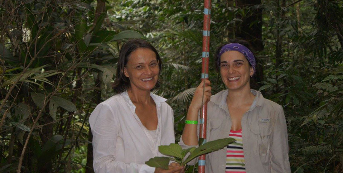 two woman hold a tall pole and leaves while doing fieldwork