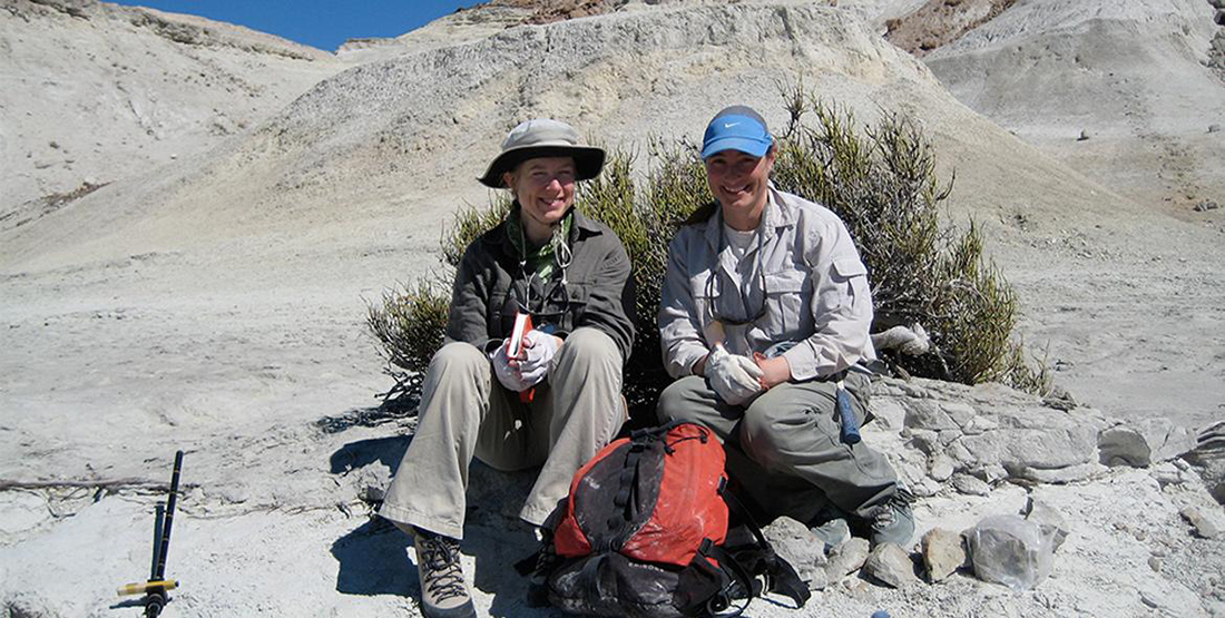 Two researchers sit with their backpacks in the desert