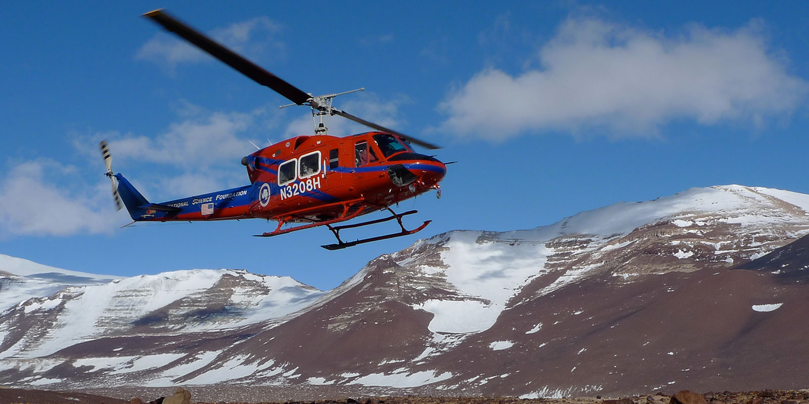 A helicopter takes off with the barren Antarctic skyline in the background