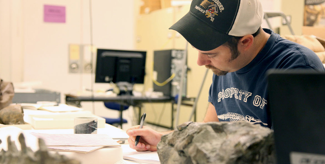 a young man writes in a field notebook while studying fossils in the Burke collection