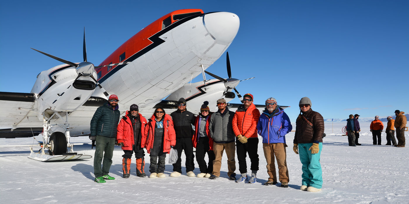 group of scientists stand in front of the airplane that dropped them off on the snow-covered runway in Antarctica