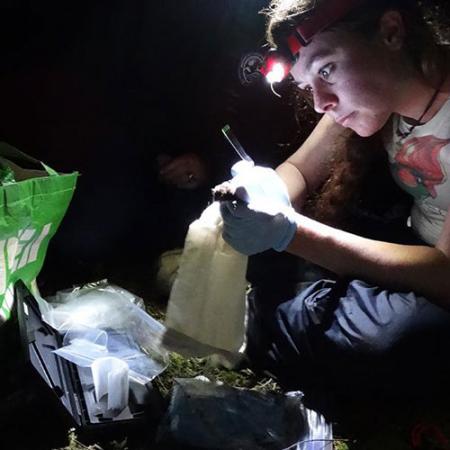 a young woman wears a headlight and holds a bat while working in the field at night