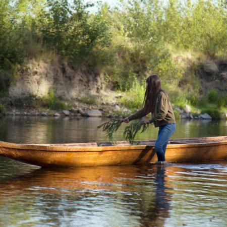 a young woman lays cedar branches in a cedar canoe in the water