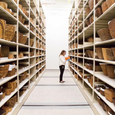 a woman stands in a row of basketry on collections shelves