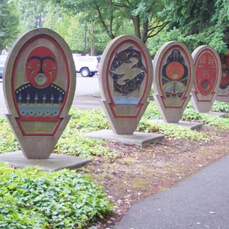 Six spirit board sculptures outdoors depicting art in the Coast Salish style