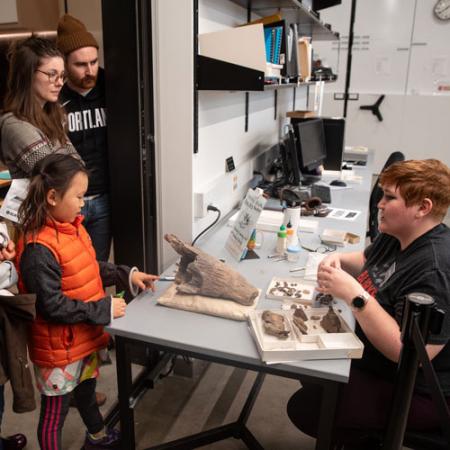 visitors stand near the open door and talk to a volunteer with fossils out on the table