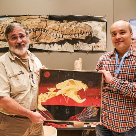 two men hold a scientific illustration in the burke's paleontology prep lab