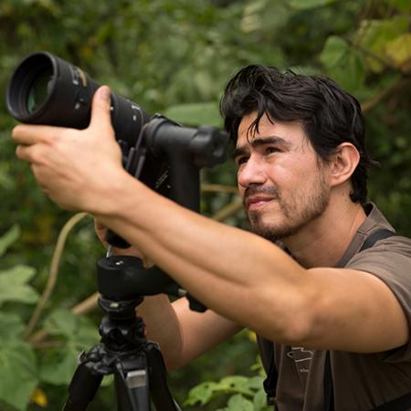 A man stands in the jungle holding a large camera