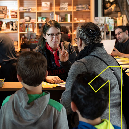 a woman holds up two fingers while describing membership to visitors