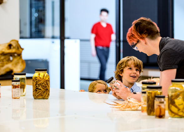 a young boy and girl speak with a burke volunteer and look at fish specimens in jars