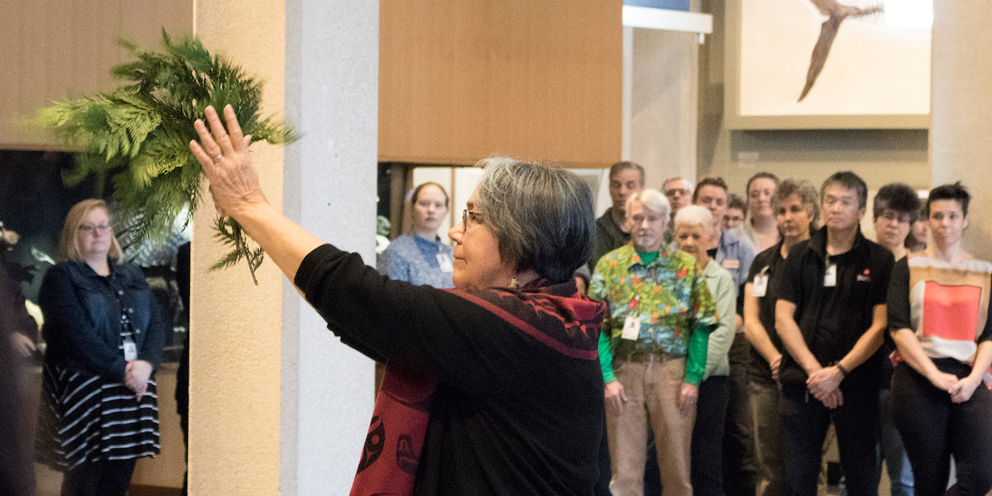 Tribal elder with cedar branches as staff stand around in circle