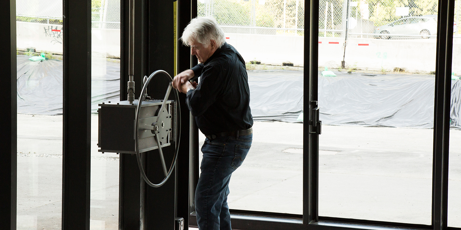 A man turns the wheel crank that opens the pivoting window wall