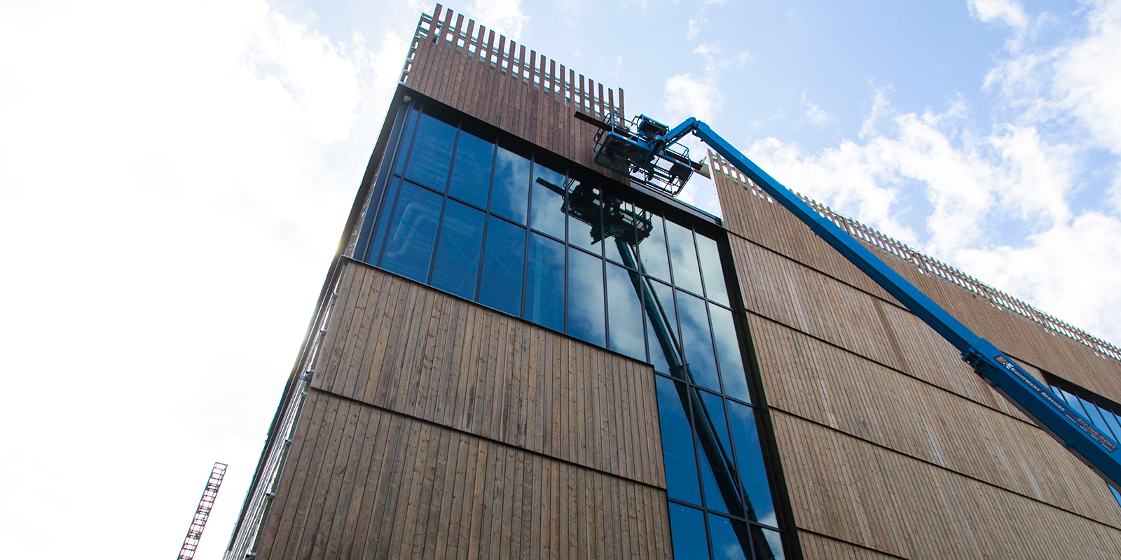 A crew member uses a lift to install siding with the lift reflecting in the glass