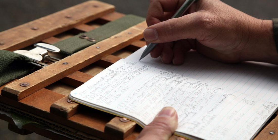 A person's hand writing field notes about the madrone specimen