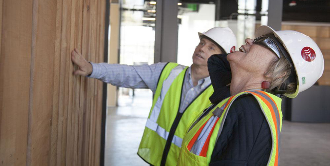 Two people wearing hard hats admire the wood planks lining the entrance to the new Burke