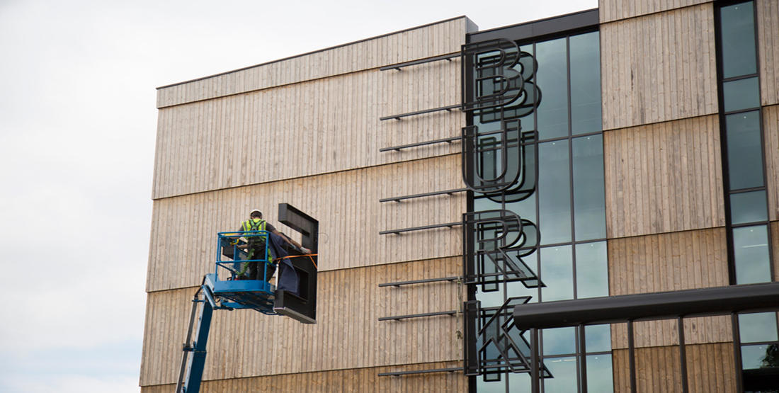 Two crew members use a lift to install the letter E on the new Burke sign