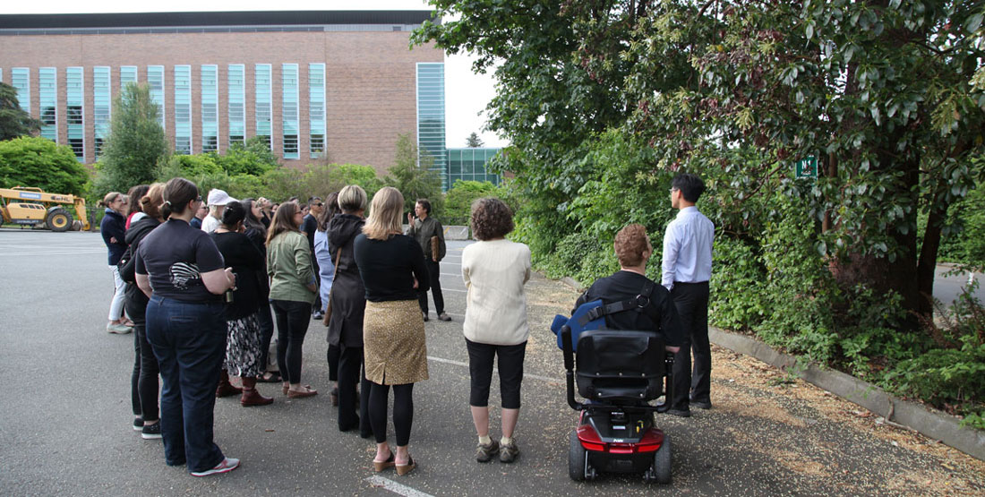 A group of people stand next to madrone trees in a parking lot