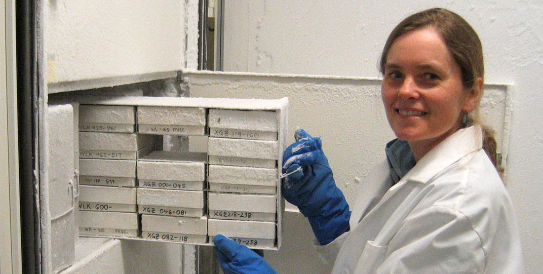 A woman researcher in a lab coat opens a cabinet drawer covered in frost