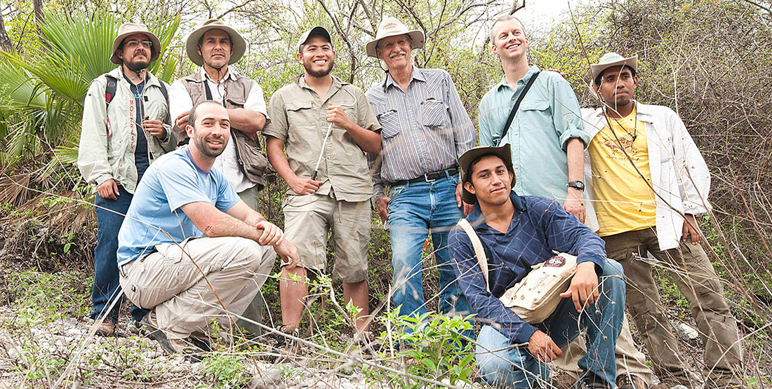 A group of 8 professors and students pose for a photo in the field 