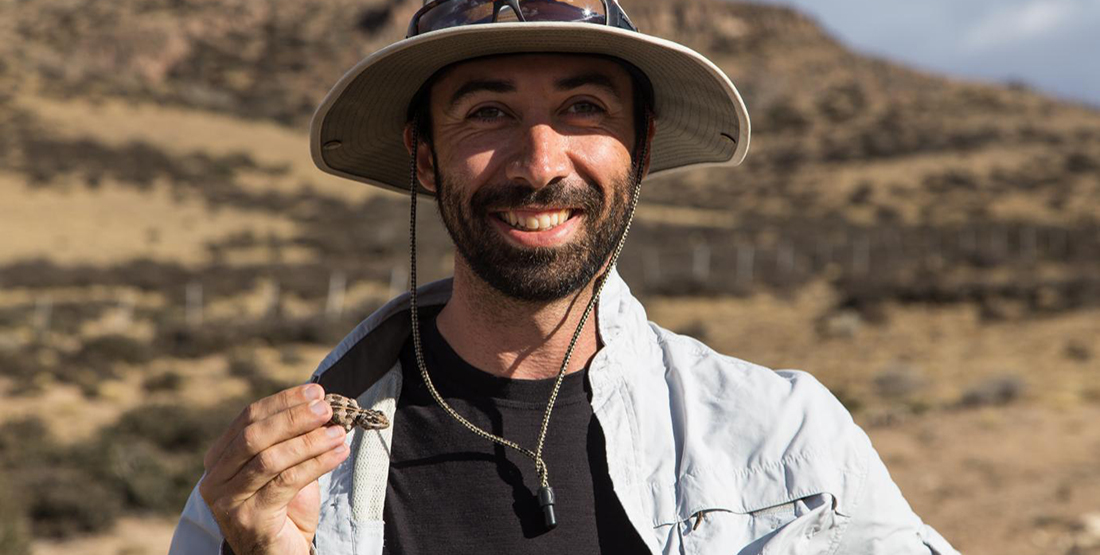 a young man holds a small lizard while researching in the field