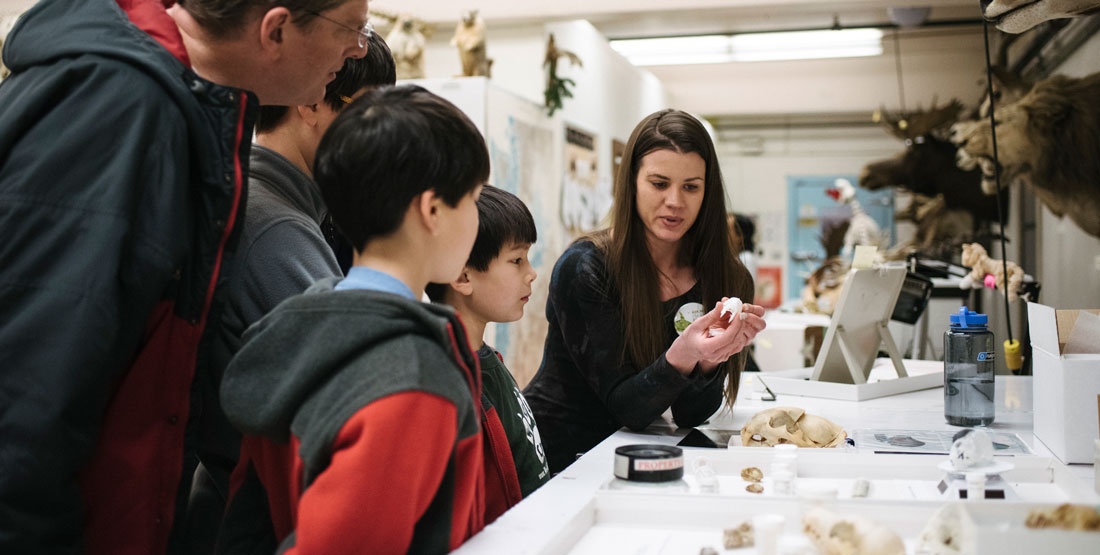 a young woman holds a bat specimen while pointing out its features to a family