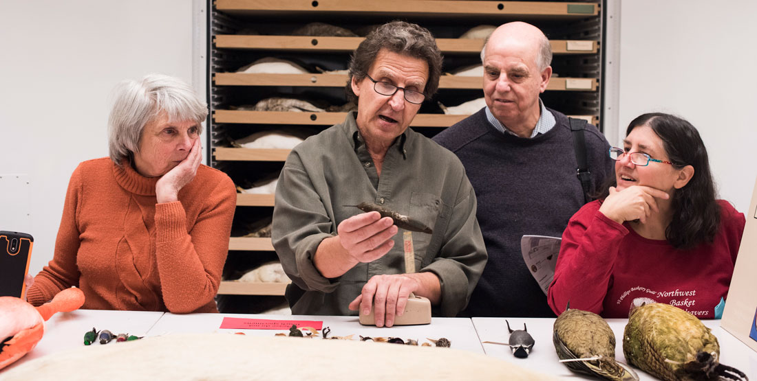 a man and two women look closely at a bird specimen being held by another man