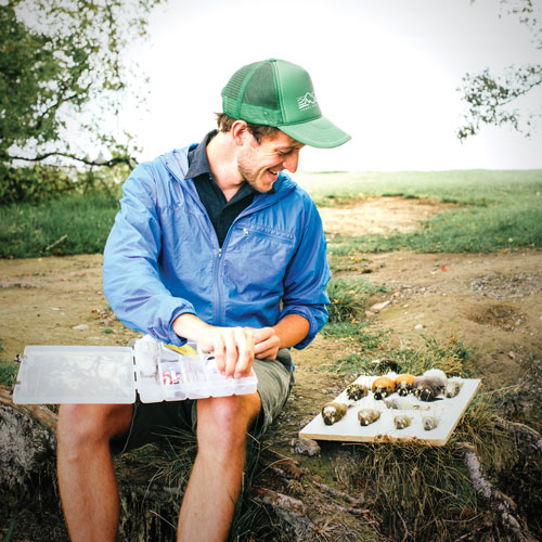 a young man sits with his field tools on his lap and bird specimens next to him