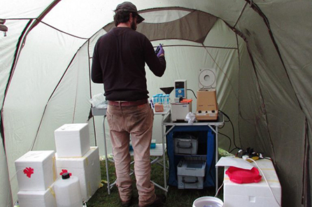 a man stands in a tent surrounded by field-based DNA testing equipment