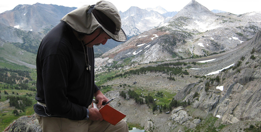 A man in the field writing in his field notebook