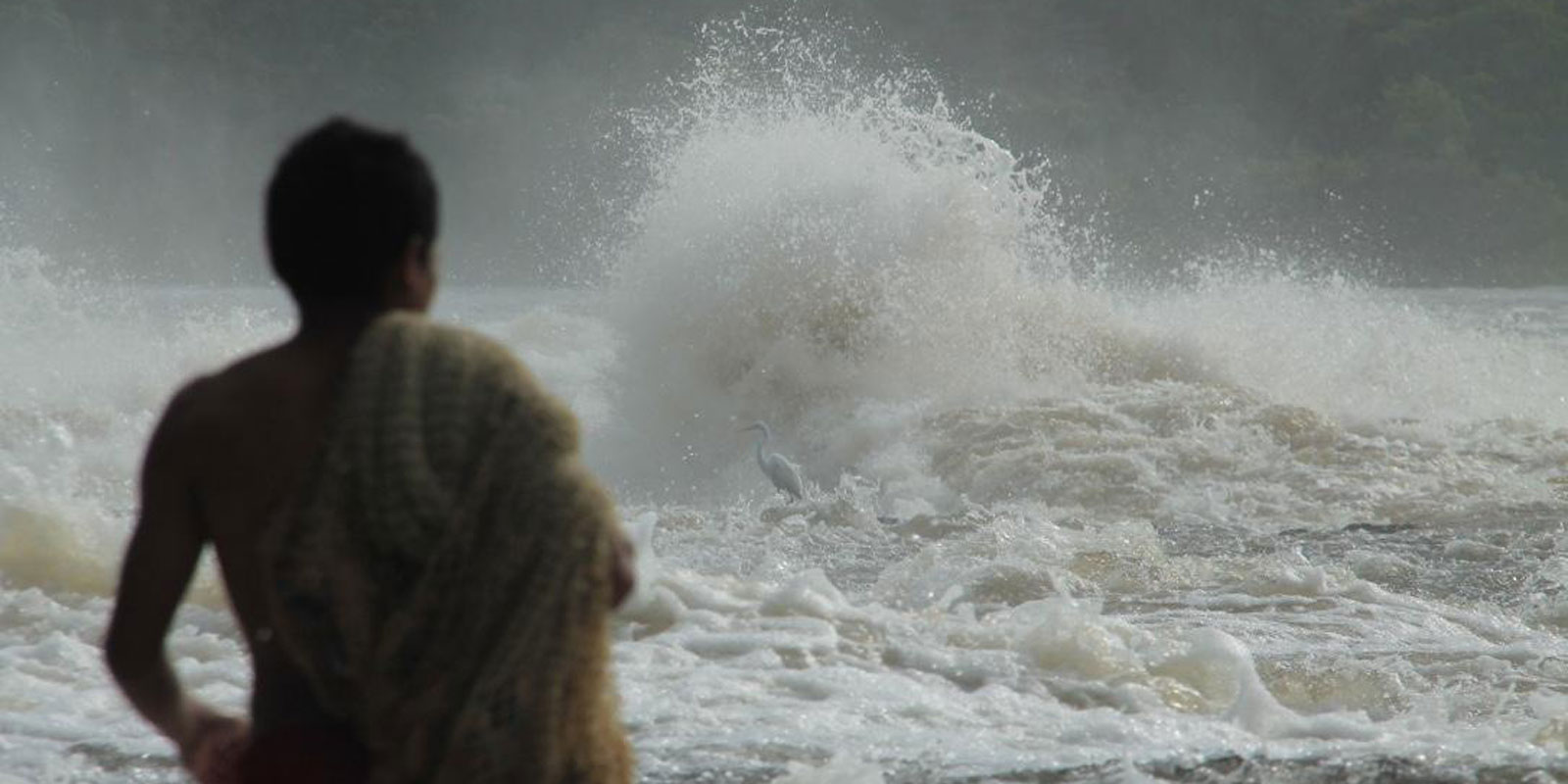 A man stands in front of a large rapid spraying water into the air