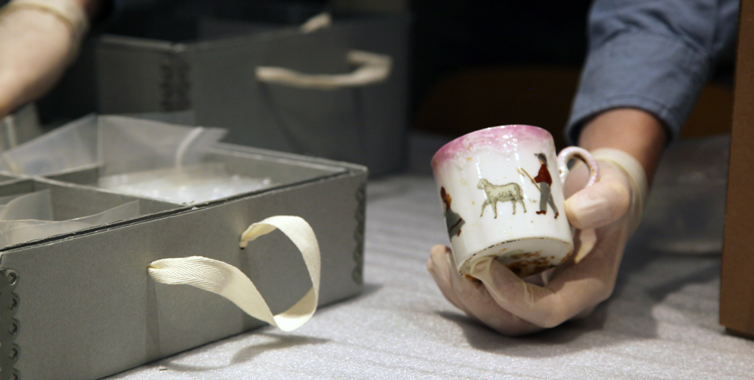 A person holds a mug with colorful paintings of people and a sheep