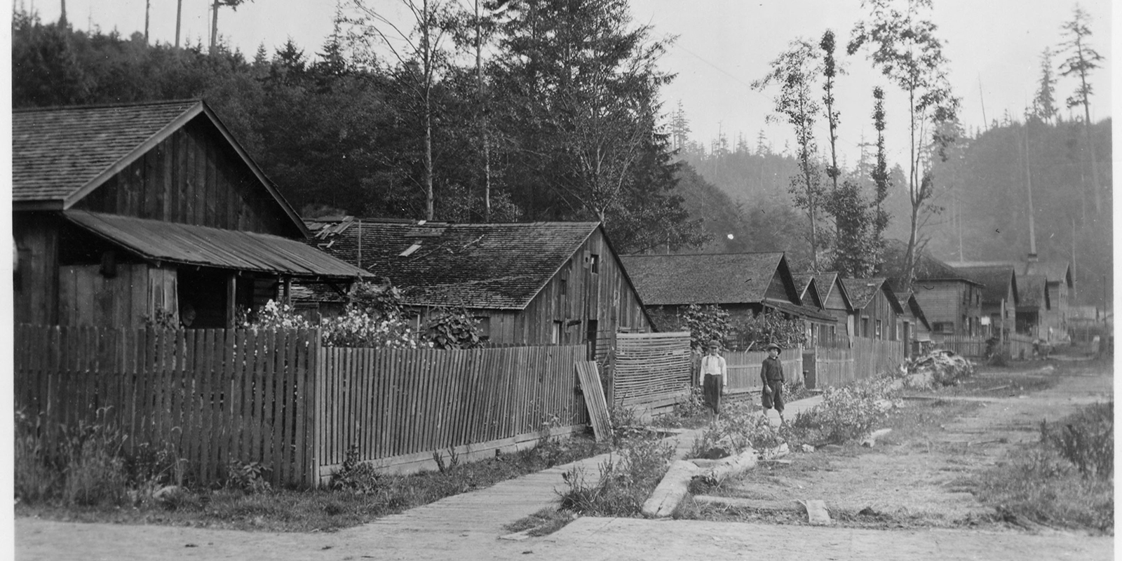 A 1922 photo of woden houses in a row with two people standing in front of the houses