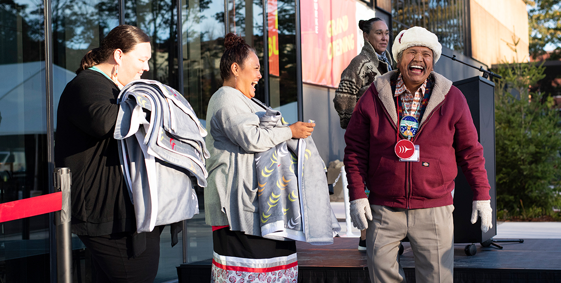 four people holding blankets and smiling in front of the new burke museum building