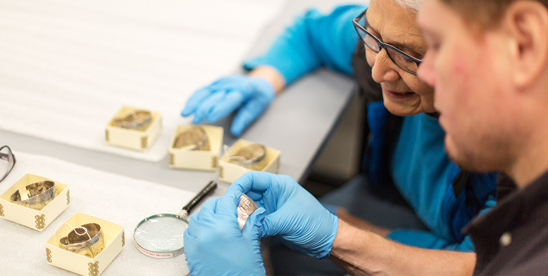 Two people examine silver bracelets