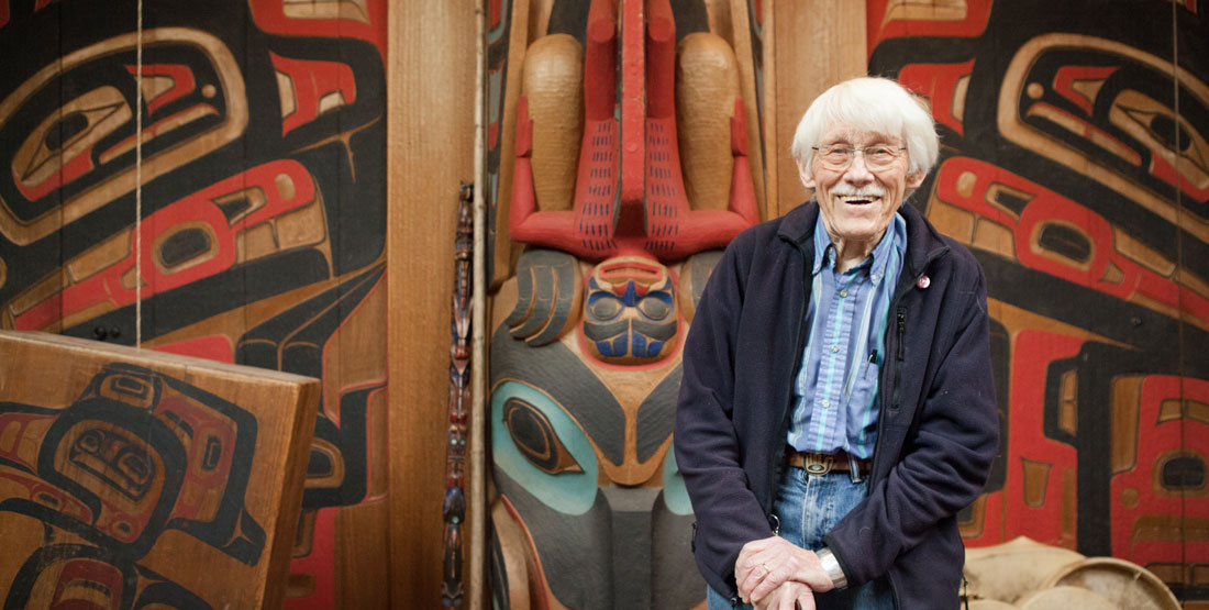 an older man stands in front of his carvings inspired by Northwest Native Art