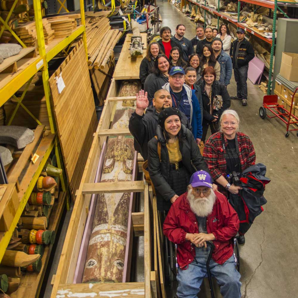 A large group stands next to the story pole after it arrived in its shipping crate to the Burke Museum collections.