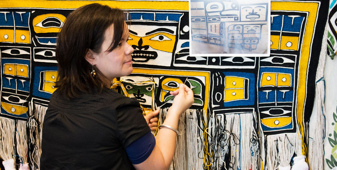 a woman sits next to a chilkat blanket she's creating