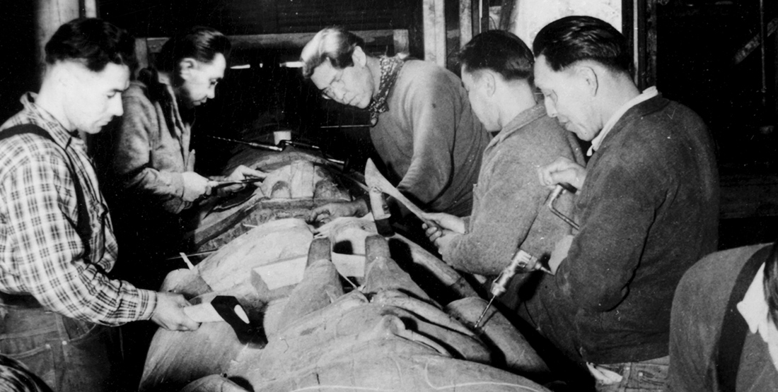 a black and white historic photo of group of men working on a totem pole